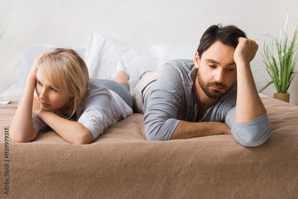 Unhappy sad couple, brunette man, cute woman, husband and wife lay on home bed, turned away from each other. Unlove crisis, sexual problem issues, relationship conflict, divorce people - concept image