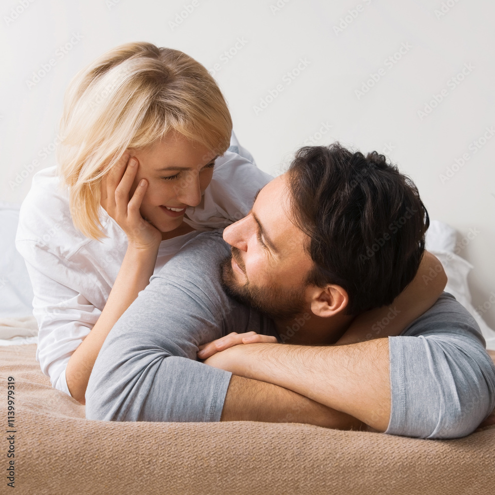 Portrait image - young playful couple looking at each other, lay on bed. Blond cute woman, brunette bearded man in love, relationship, dating, happy family, comfortable rest time concept. Square. Portrait image - young playful couple looking at each other, lay on bed. Blond cute woman, brunette bearded man in love, relationship, dating, happy family, comfortable rest time concept. Square.