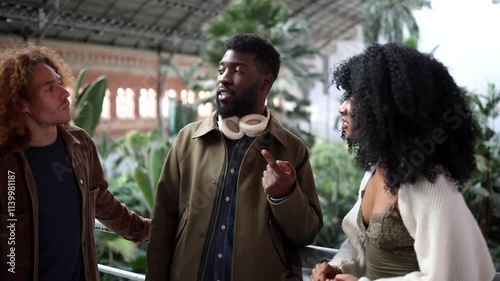 Three young multi ethnic friends, two men and a woman, are walking and talking together inside the atocha railway station in madrid, spain, enjoying their time together before taking the train