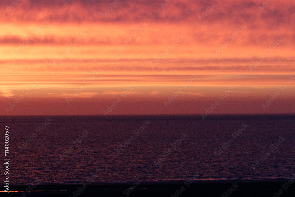Fototapeta premium Sunset over a calm sea. Vibrant hues of orange and red paint the sky, reflecting on the dark water. Tranquil scene.