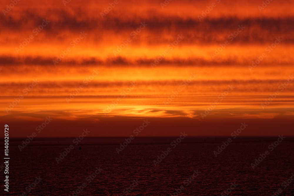 Obraz premium Fiery orange sunset over dark water. Silhouette of a buoy on the horizon. Dramatic colors.
