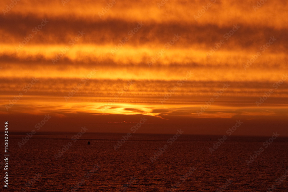 Fiery orange sunset over a calm, dark ocean. Striated clouds paint the sky. Tranquil scene. Fiery orange sunset over a calm, dark ocean. Striated clouds paint the sky. Tranquil scene.