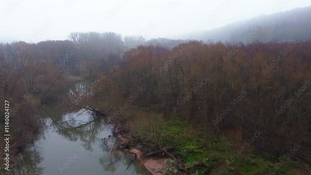 A quiet river winds through a misty forest of bare and colorful trees, blending into a foggy horizon. A tranquil late autumn scene in rural Germany. A quiet river winds through a misty forest of bare and colorful trees, blending into a foggy horizon. A tranquil late autumn scene in rural Germany.
