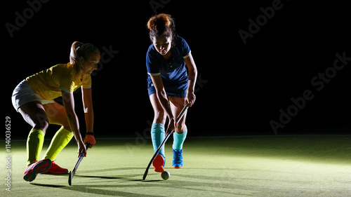 Female players engage in competitive field hockey match in contrast studio light