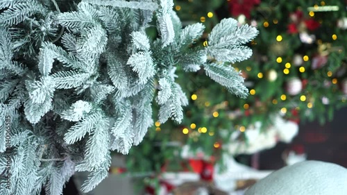 vertical video with snow-covered branches of a Christmas tree against the background of shimmering bokeh from garlands and a blurred silhouette of Santa Claus fulfilling children's wishes