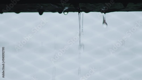 Rain water is flowing doen from the edge of the roof during heavy rainfall, with bright blurry natural background. photo