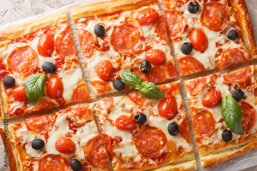 Obraz na płótnie Tasty baked Puff pastry tart pizza style with pepperoni sausage, olives, tomatoes and mozzarella cheese close-up on parchment on table. Horizontal top view from above w salonie