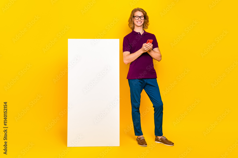 Full size photo of cheerful satisfied person stand near huge phone isolated on yellow color background Full size photo of cheerful satisfied person stand near huge phone isolated on yellow color background