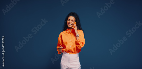 Woman engaging in communication on mobile phone with bright orange and blue color blocking background