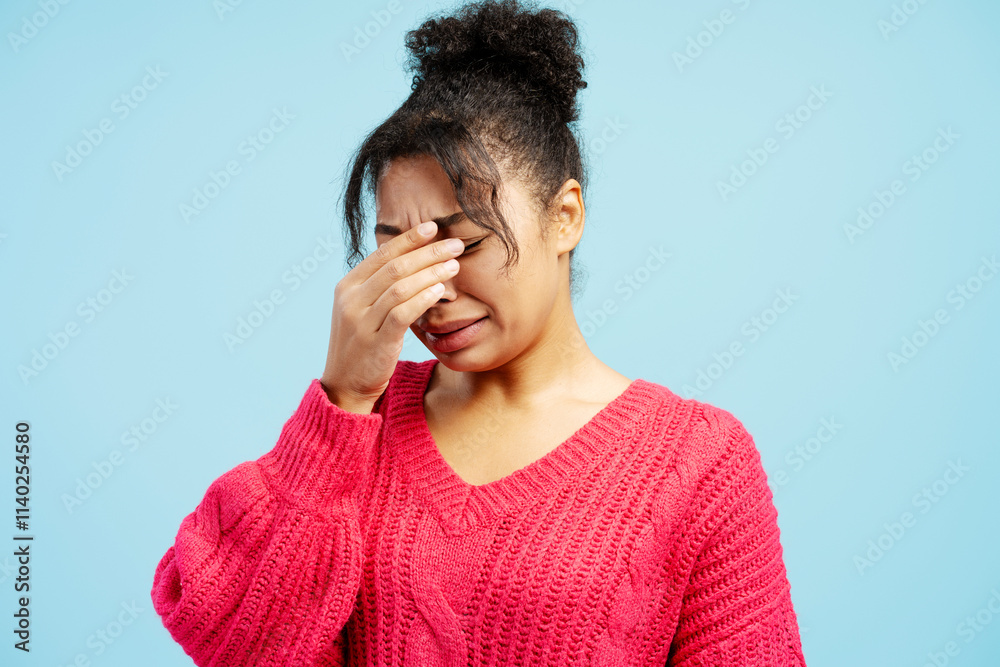 Young woman crying and touching her face on blue background Young woman crying and touching her face on blue background