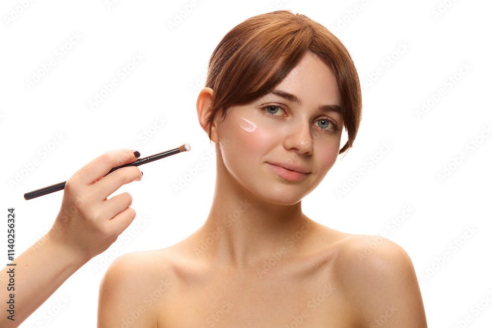 Young beautiful woman applying skincare cream to her face using makeup brush, promoting beauty and self-care routines against white background. Concept of natural beauty, cosmetics and cosmetology Young beautiful woman applying skincare cream to her face using makeup brush, promoting beauty and self-care routines against white background. Concept of natural beauty, cosmetics and cosmetology