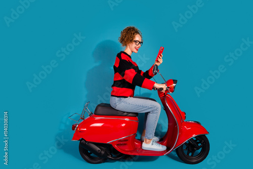 Young woman on a red scooter taking a selfie with blue background and striped sweater photo