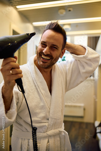 Cheerful man blow-drying his hair and looking at camera. photo