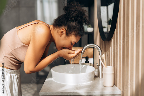 Foto Young woman washing face at bathroom sink