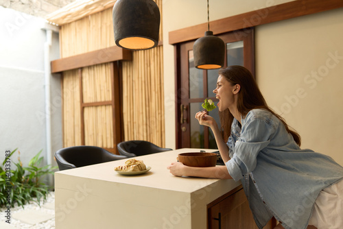 Young woman enjoying healthy green food in a bright modern kitchen, expressing happiness and freshness, with wooden elements and natural light