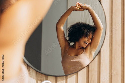 Happy black woman stretching arms looking in bathroom mirror photo