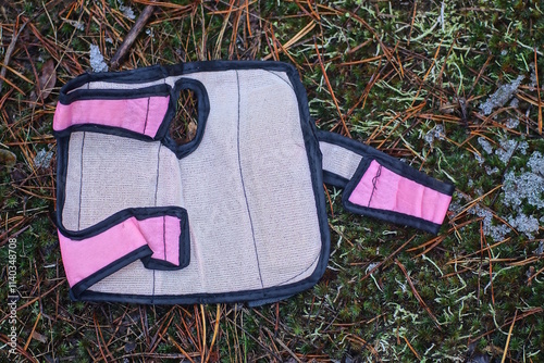 one grey square knee pad with pink straps lies on the ground and green moss in the street