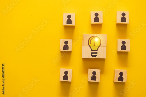 Wooden blocks with people icons surrounding a central light bulb block, symbolizing teamwork, innovation, and collaborative ideas.
