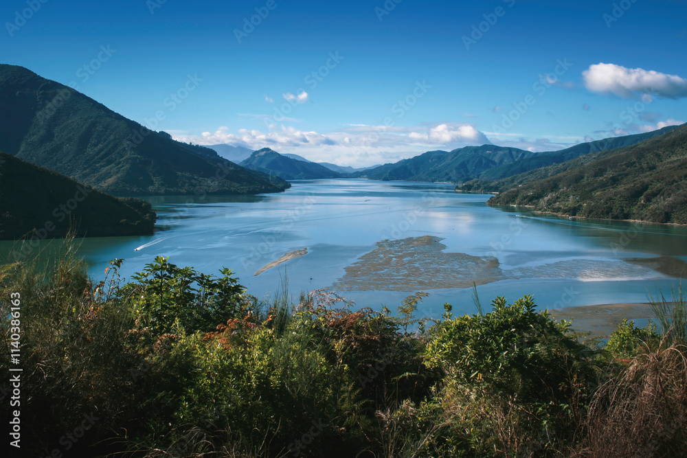 Obraz premium Tranquil landscape of Pelorus Sound in Marlborough Sounds, New Zealand, with blue tidal water, calm pacific ocean, distant mountains and valley, dramatic clouds on a clear sunny day