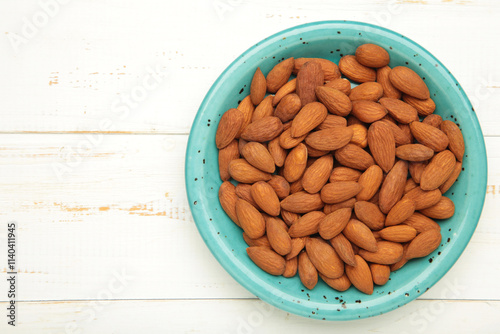 Fresh natural healthy almonds nuts in blue plate on white wooden background.