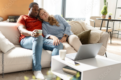African American man with coffee watching film on laptop while woman sleeping near him