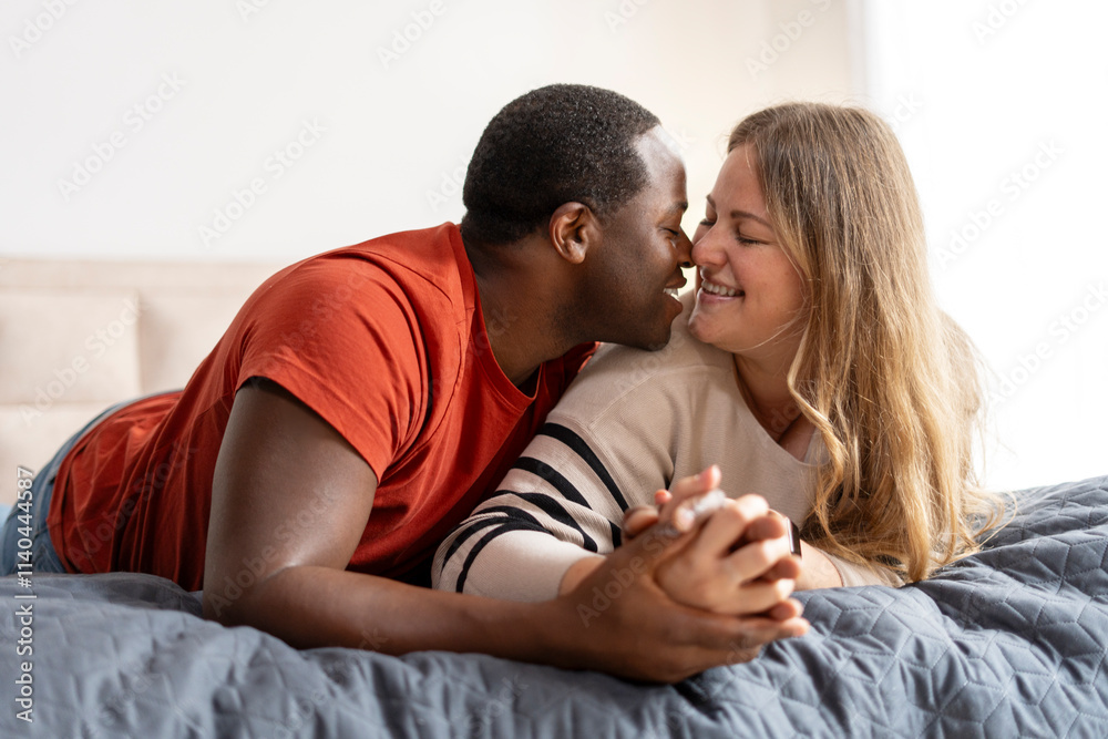 Obraz premium Happy romantic couple holding hands, lying on bed and kissing
