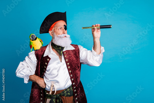 Photo of senior funny pirate grandpa hold binoculars tube look empty space wear masquerade party costume isolated blue color background photo