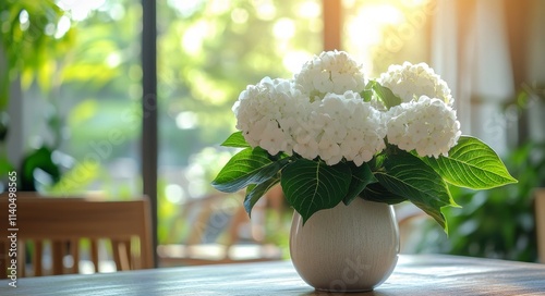 White flowers in a vase on a wooden table surrounded by greenery indoors