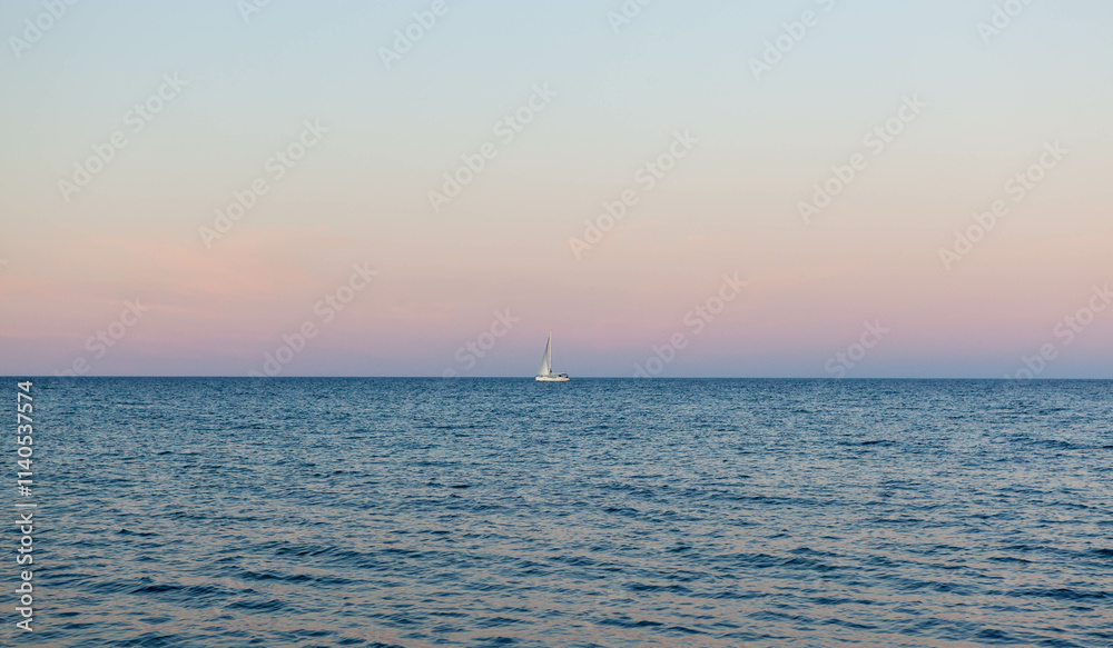 Single white sailboat at the horizon in the sea at sunset. Yacht in the Mediterranean sea. Single white sailboat at the horizon in the sea at sunset. Yacht in the Mediterranean sea.