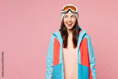 Skier young shocked surprised woman wear warm blue padded jacket ski goggles mask spend extreme weekend winter season in mountains look aside on area isolated on plain pink background. Hobby concept. photo