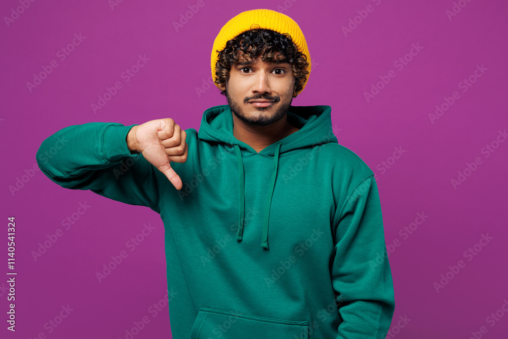 © ViDi Studio - Young sad disappointed dissatisfied Indian man he wear green hoody yellow hat casual clothes showing thumb down dislike gesture isolated on plain purple background studio portrait. Lifestyle concept. © ViDi Studio - Young sad disappointed dissatisfied Indian man he wear green hoody yellow hat casual clothes showing thumb down dislike gesture isolated on plain purple background studio portrait. Lifestyle concept.