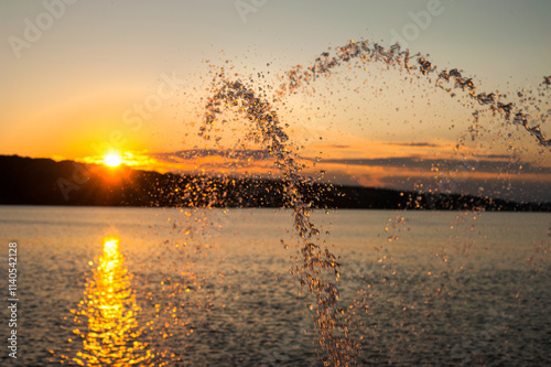 fountains on a pond illuminated by sunlight at sunset in a city park on a sum...