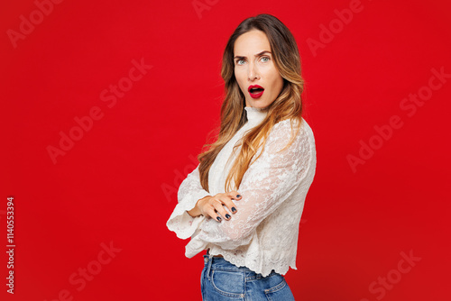 Side profile view young sad frowning Caucasian woman she wearing white blouse casual clothes hold hands crossed folded look camera isolated on plain red background studio portrait. Lifestyle concept. photo