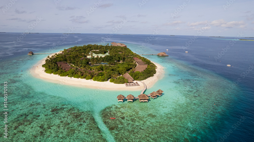 Turquoise clear water and the green island of Maldives. Top view of the ocean and the reef. Palm trees grow on the island. There are bungalows and villas. White sand on the beach. Fish are visible
