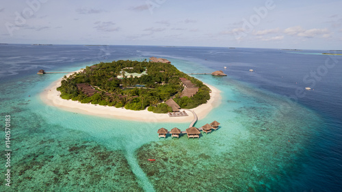 Obraz na płótnie Turquoise clear water and the green island of Maldives. Top view of the ocean and the reef. Palm trees grow on the island. There are bungalows and villas. White sand on the beach. Fish are visible w salonie