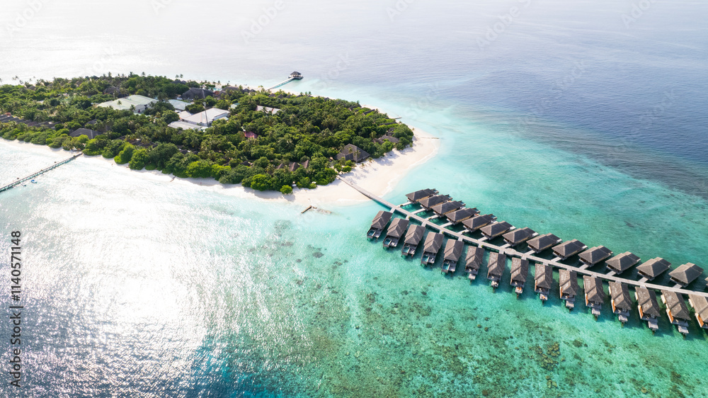 Top view of the bungalow on the water. Maldives. Luxury villas near the green island. The view from the drone. Turquoise water, beautiful reef. The rays of the sun on the surface of the ocean. Waves