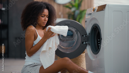 African American female woman girl ethnic lady housewife homeowner housework at floor open washing machine smell clean white towel cloth bad smelling sniff terrible aroma laundry conditioner gel stink