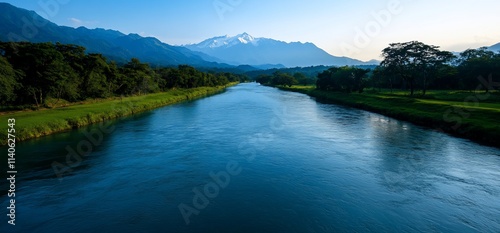 Serene river flowing through lush green landscape with majestic mountains in the background.