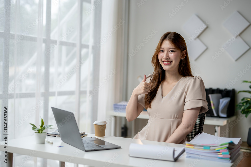 A woman is sitting at a desk with a laptop and a cup of coffee