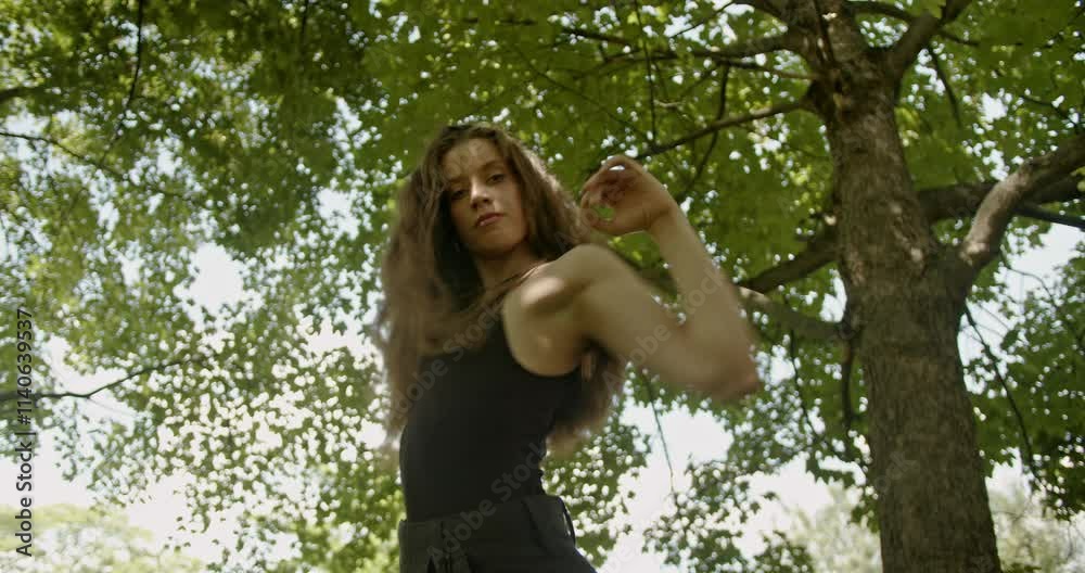 A young woman gracefully dances modern dance in a sunny forest, expressing herself through movement. A young woman gracefully dances modern dance in a sunny forest, expressing herself through movement.