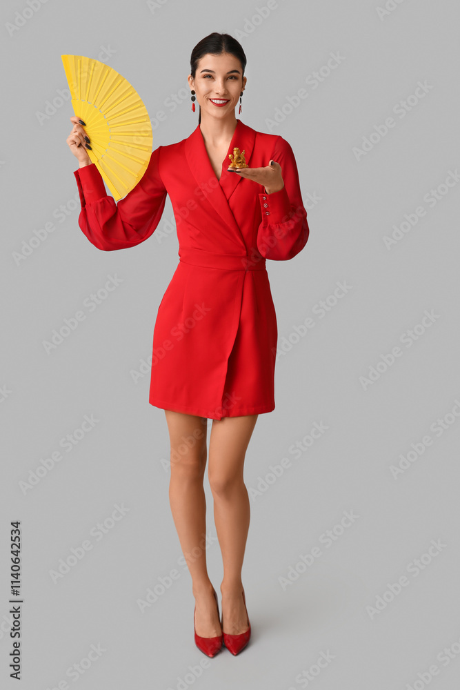 Beautiful young happy woman with golden dragon figurine and fan on grey background. Chinese New Year celebration Beautiful young happy woman with golden dragon figurine and fan on grey background. Chinese New Year celebration