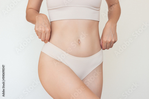 A shoot of a young slim Caucasian woman in beige underwear posing for the camera. Beauty, sports, and a healthy body