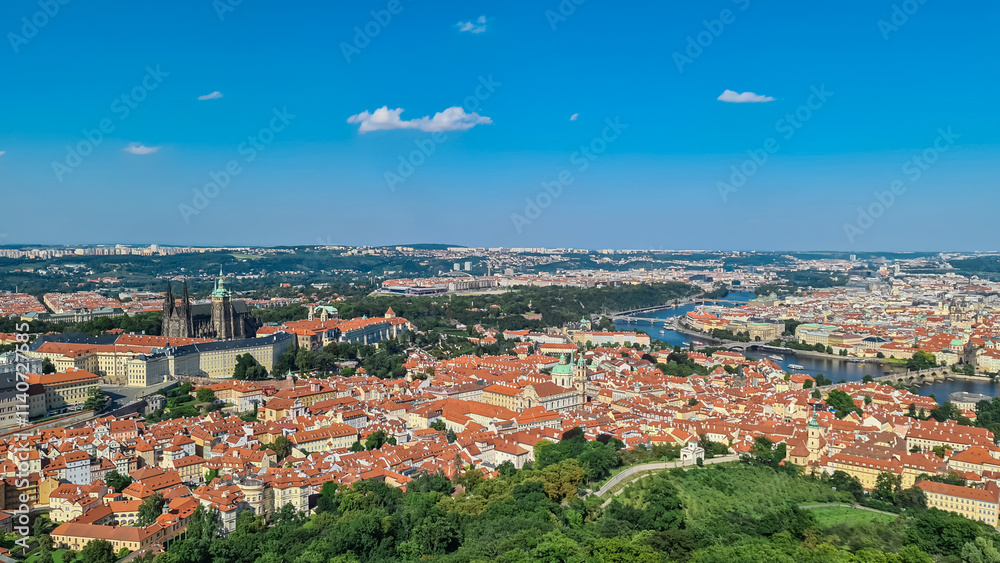 Obraz premium Aerial view of Prague seen from Petrin tower, Czechia. City's iconic landmarks, including Prague Castle, St. Vitus Cathedral and Charles Bridge are visible in distance. Vltava River winds through city