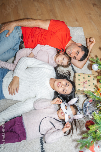 The family enjoys quality time near the decorated Christmas tree. The children unwrap presents, play, and cherish the festive atmosphere of Christmas and New Year.