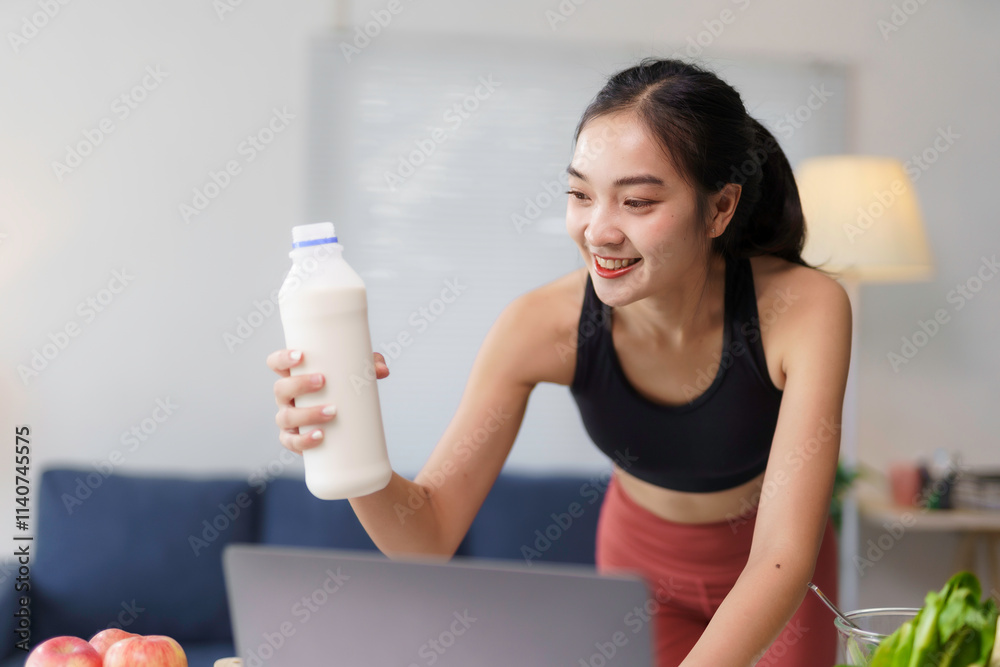 Young sportswoman showing a bottle of milk while attending a workout session online at home Young sportswoman showing a bottle of milk while attending a workout session online at home