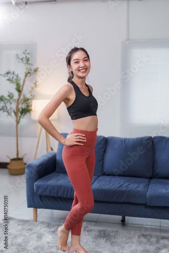 Fit asian woman wearing sportswear, smiling and posing confidently in her living room, promoting a healthy and active lifestyle