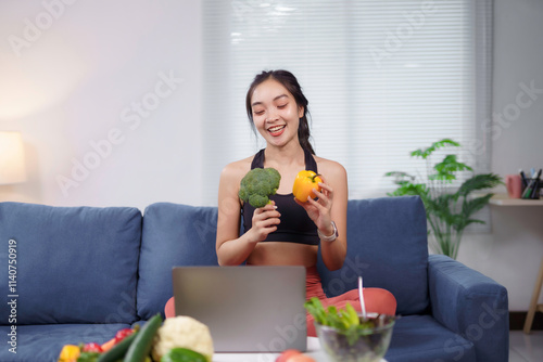 Asian nutritionist holding broccoli and bell pepper while giving online consultation through video call at home photo