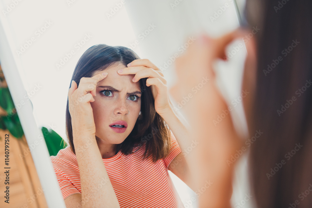 Fototapeta premium Young woman examining her skin in front of a mirror in a bright, cozy living room during the day
