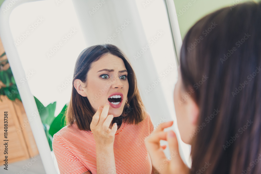 Young woman examining her skin in mirror with concerned expression in bright living room Young woman examining her skin in mirror with concerned expression in bright living room