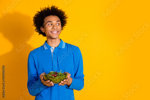 Photo of nice young man hold salad look empty space wear blue shirt isolated on yellow color background photo